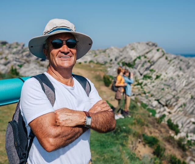 man hiking wearing hat, sunglasses, and backpack